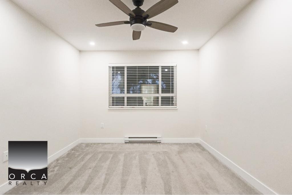 Bright, empty room with white walls, a ceiling fan, and a large window in a Surrey condo at 410-15895 84th Ave.