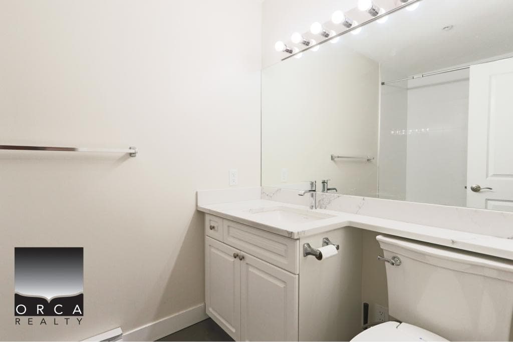 Bright bathroom featuring a white vanity with a large mirror, modern fixtures, and a clean, minimalist design in a Surrey condo. Perfect for comfortable living and stylish home updates.
