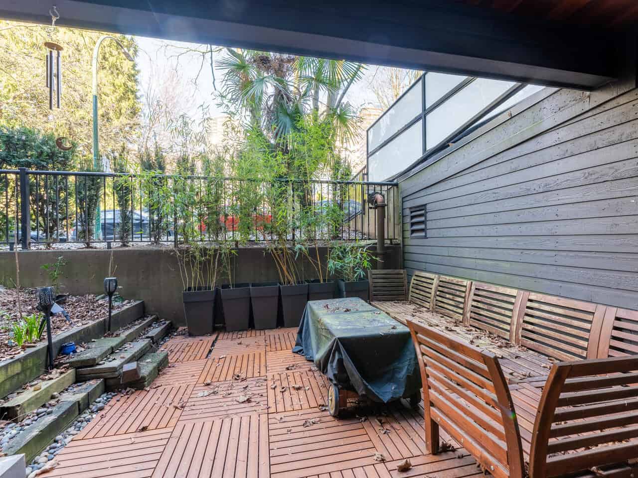 Outdoor patio space at 112-1550 Barclay St, Vancouver, featuring wooden benches, a table with a cover, and potted plants, ideal for relaxing or entertaining in a prime Vancouver location.