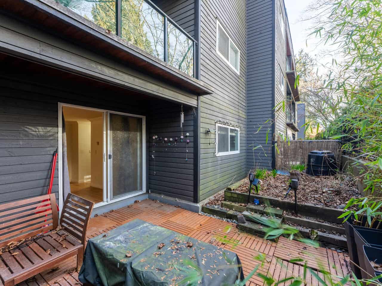 Spacious outdoor patio area of a Vancouver townhouse at 112-1550 Barclay St, featuring wooden decking, garden beds, and a cozy outdoor seating arrangement.