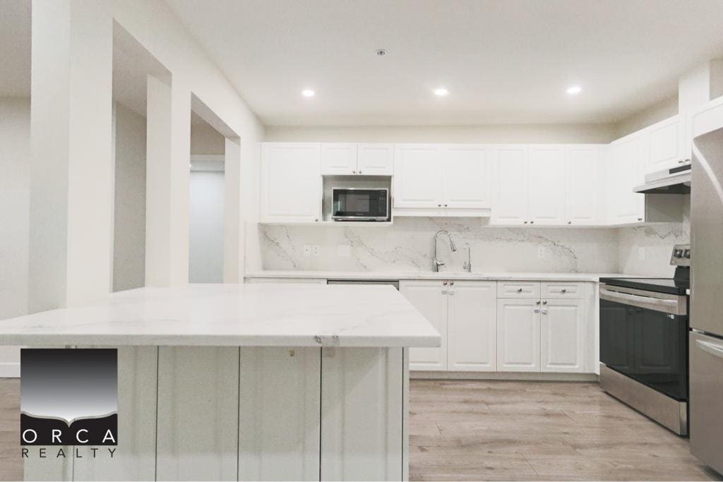 Spacious kitchen featuring sleek white cabinets, marble countertops, and stainless steel appliances in Surrey, BC. Perfect for contemporary living and entertaining.