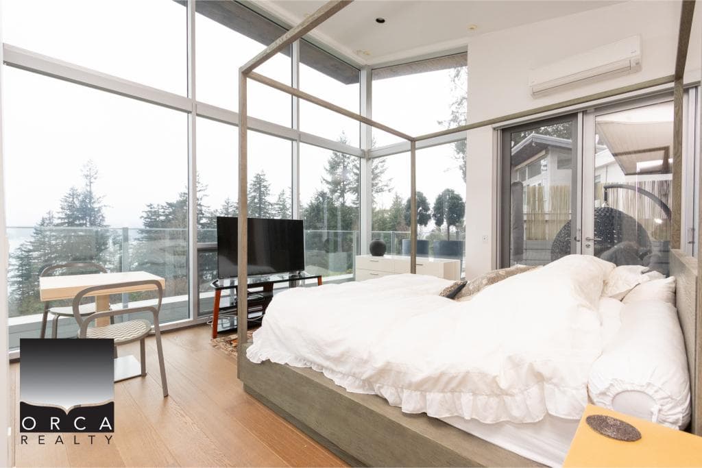 Bright, airy bedroom with large windows overlooking trees, featuring a comfortable bed and contemporary decor. Perfect for relaxing or enjoying scenic views in a stylish setting.