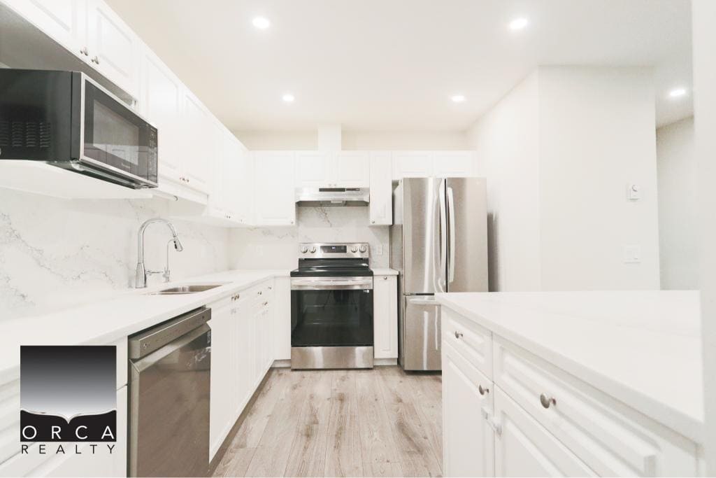 Bright and spacious kitchen featuring stainless steel stove, refrigerator, and microwave in Surrey property. Elegant white cabinetry and marble countertops create a sleek, contemporary look.