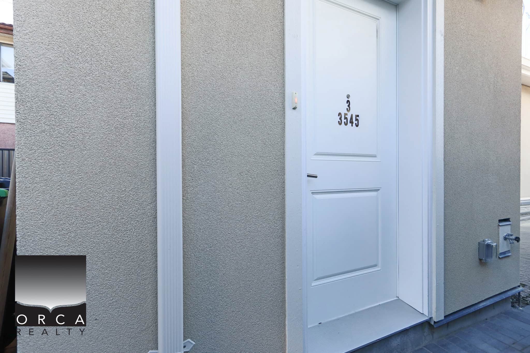 Front door of a contemporary Vancouver residence at 3-3545 East 26th Avenue, showcasing a clean, white exterior with modern design elements.