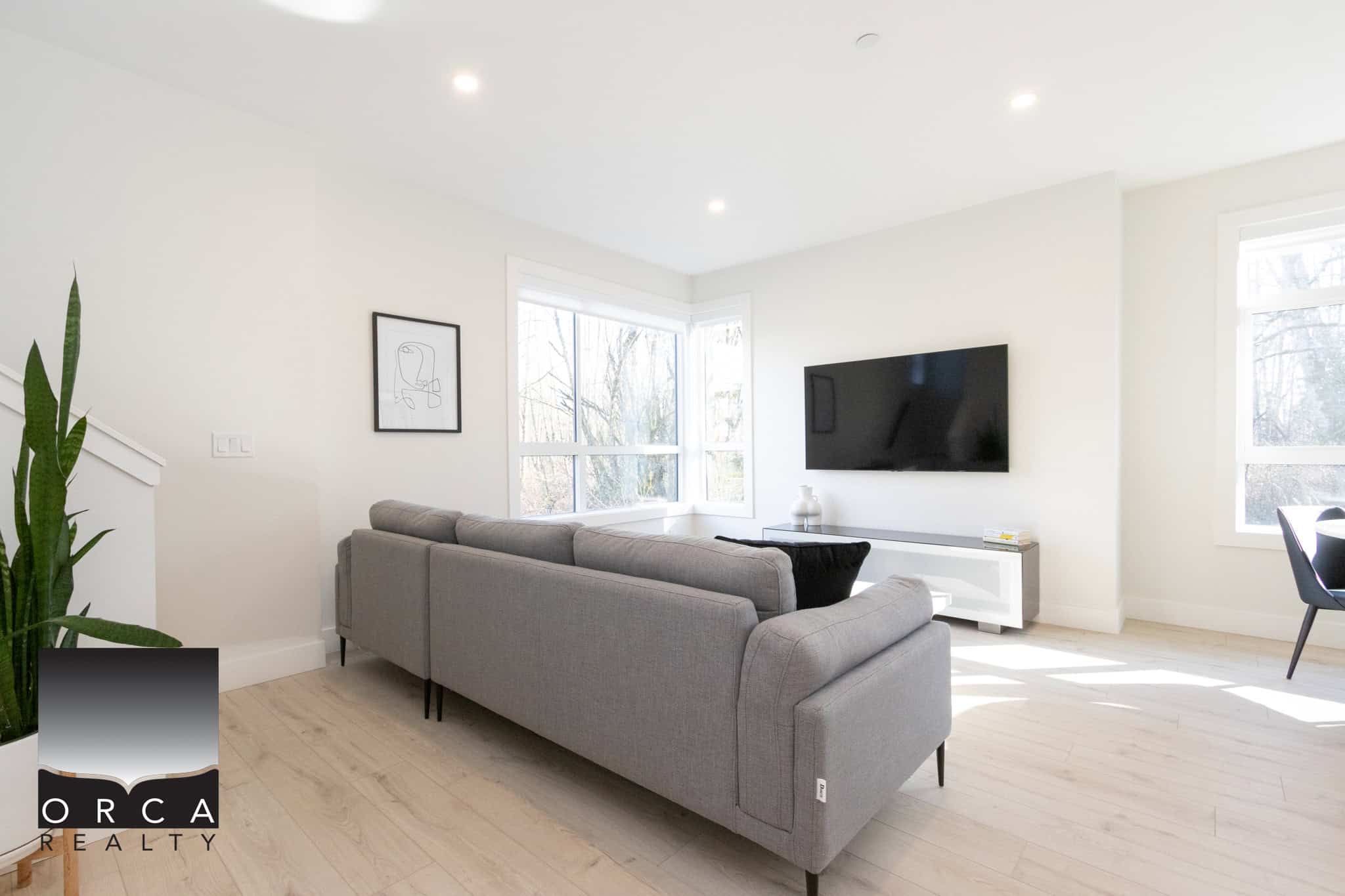 Bright and spacious living room featuring large windows, a sleek gray sofa, and a wall-mounted TV, perfect for relaxing or entertaining in Langley.