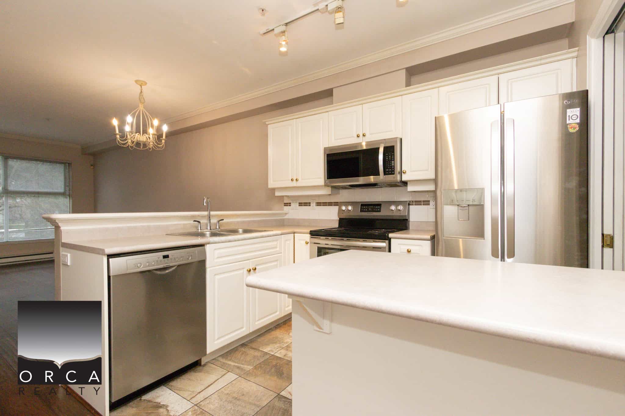 Spacious kitchen featuring stainless steel refrigerator, microwave, and dishwasher in a Coquitlam property listed by Orca Realty Inc.