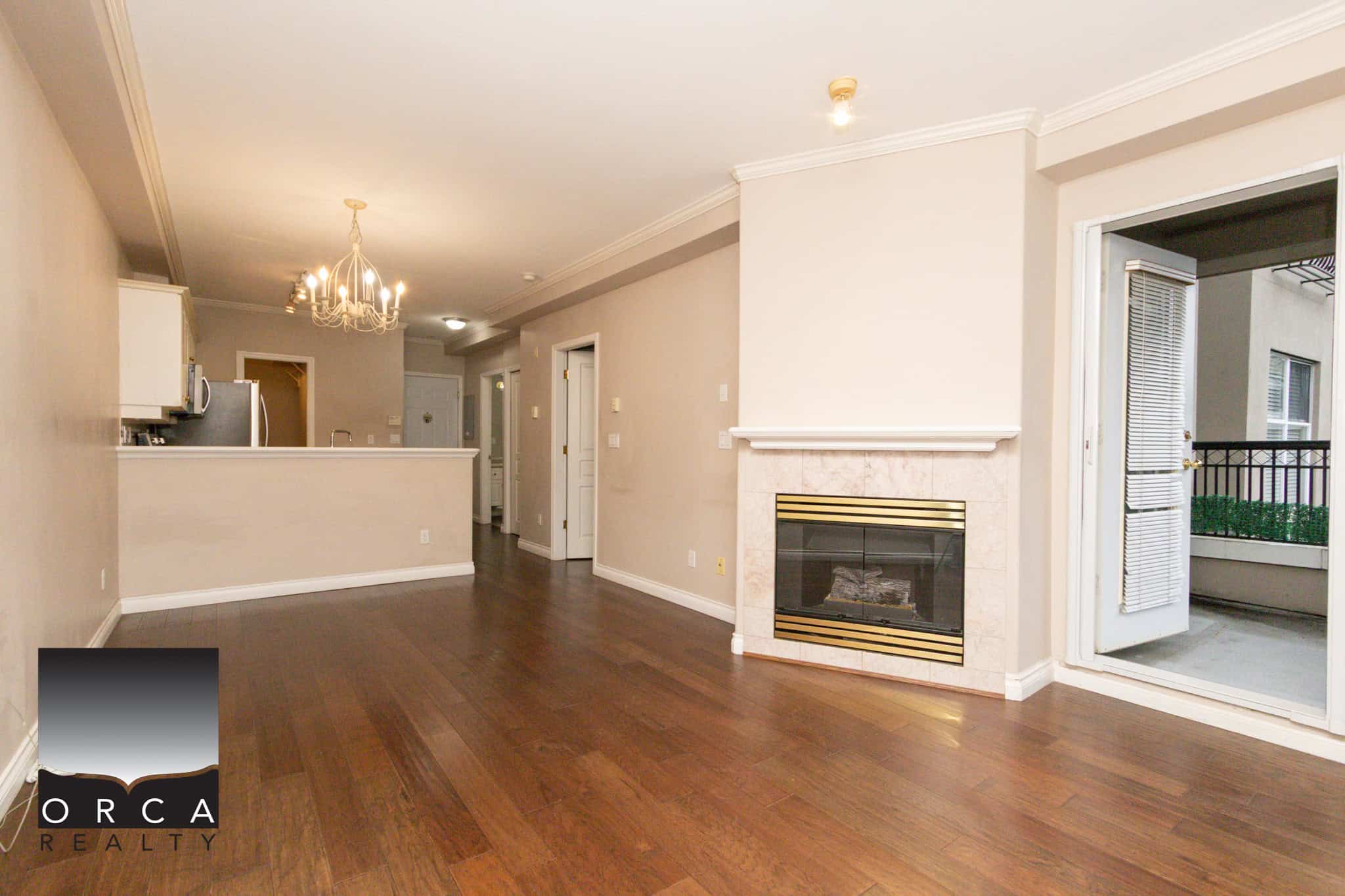 Spacious interior of 202-1185 Pacific St, Coquitlam, showcasing a bright living area with hardwood floors, a cozy fireplace, and access to a balcony, ideal for comfortable urban living.