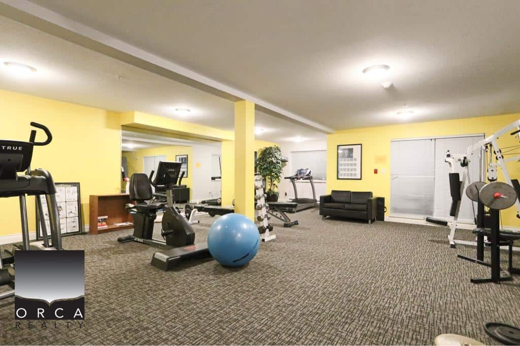 Brightly lit fitness area with gym equipment, exercise balls, and a cozy seating corner at Orca Realty Inc. in Surrey, perfect for wellness and client meetings.