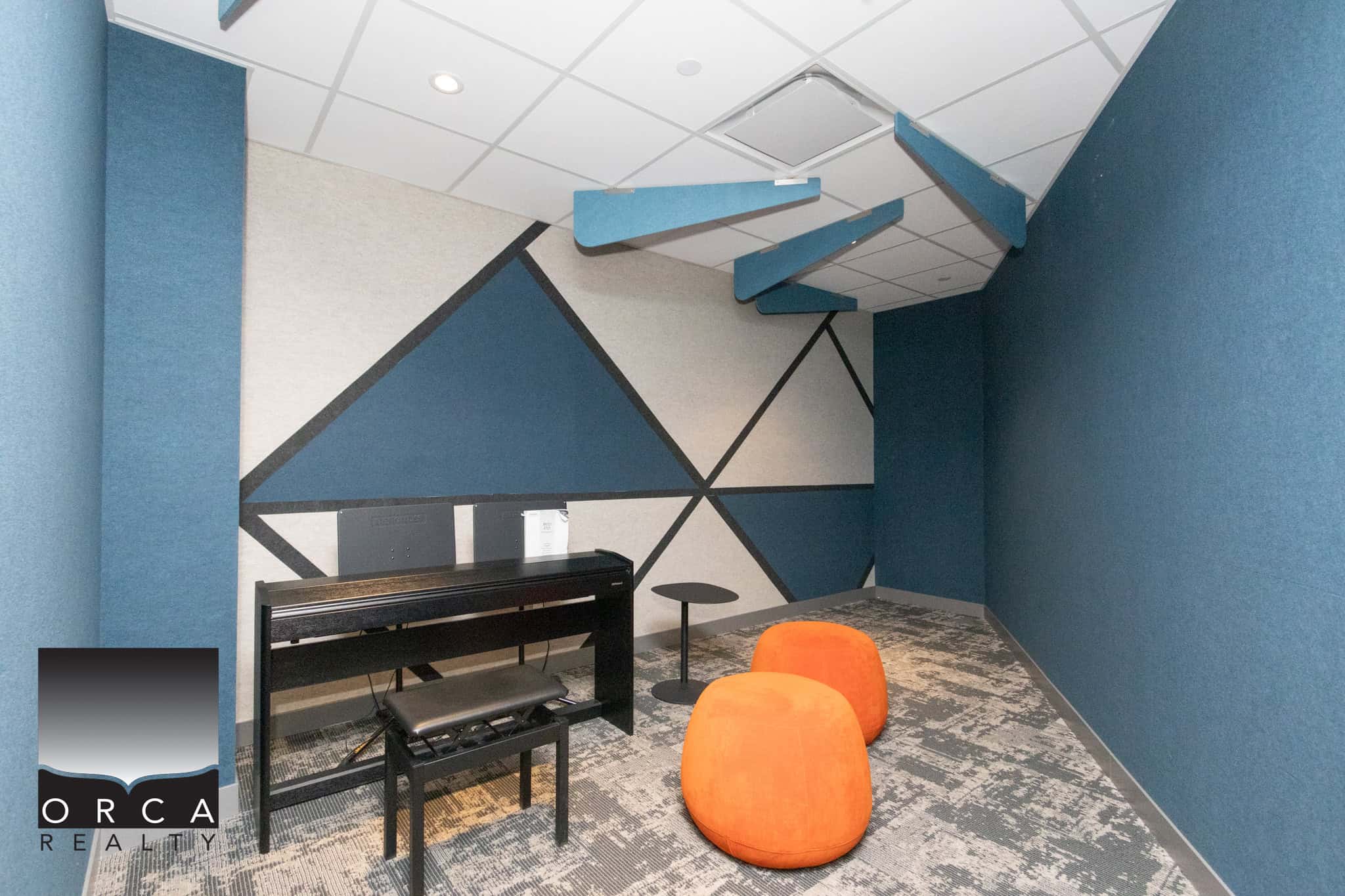 Modern Office Meeting Room with Acoustic Panels Contemporary office space featuring acoustic wall panels, a black digital piano, and vibrant orange seating for meetings or creative sessions.
