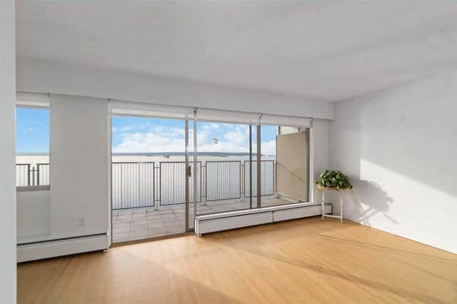 Bright living room with large glass sliding doors opening to a balcony overlooking scenic views in West Vancouver. Modern interior with hardwood floors and ample natural light.