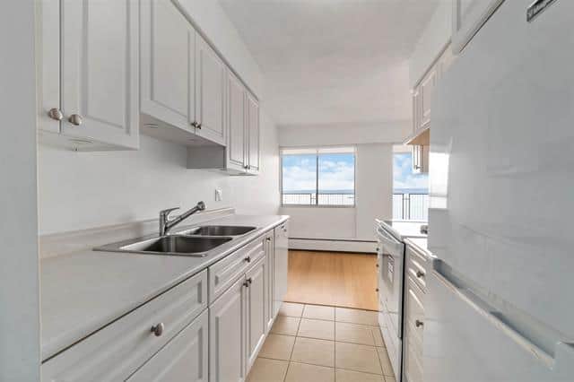 Bright kitchen with white cabinetry and stainless steel sink, overlooking the ocean in West Vancouver. Perfect for coastal living and entertaining.