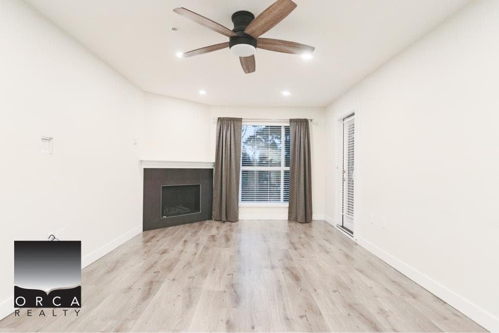 Spacious living room featuring a sleek fireplace, large windows with curtains, and a ceiling fan, perfect for comfortable living in Surrey.