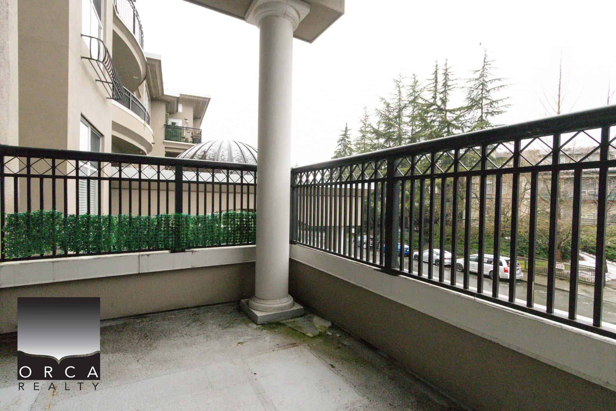 Balcony overlooking lush trees and neighboring buildings at 202-1185 Pacific St, Coquitlam, offering a peaceful outdoor space in a residential complex.