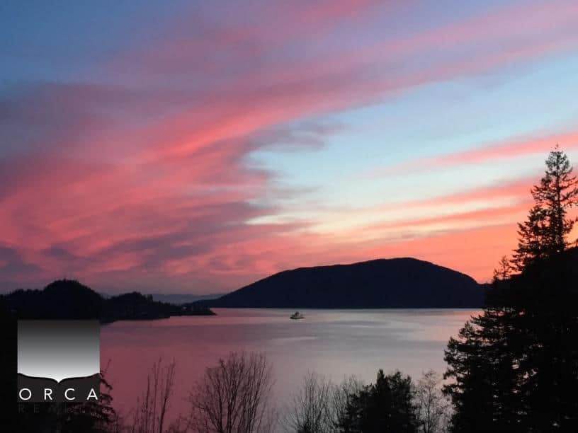 Sunset over Ansell Place with vibrant pink and blue sky reflecting on calm waters, surrounded by lush trees and distant hills, showcasing a peaceful lakeside setting.