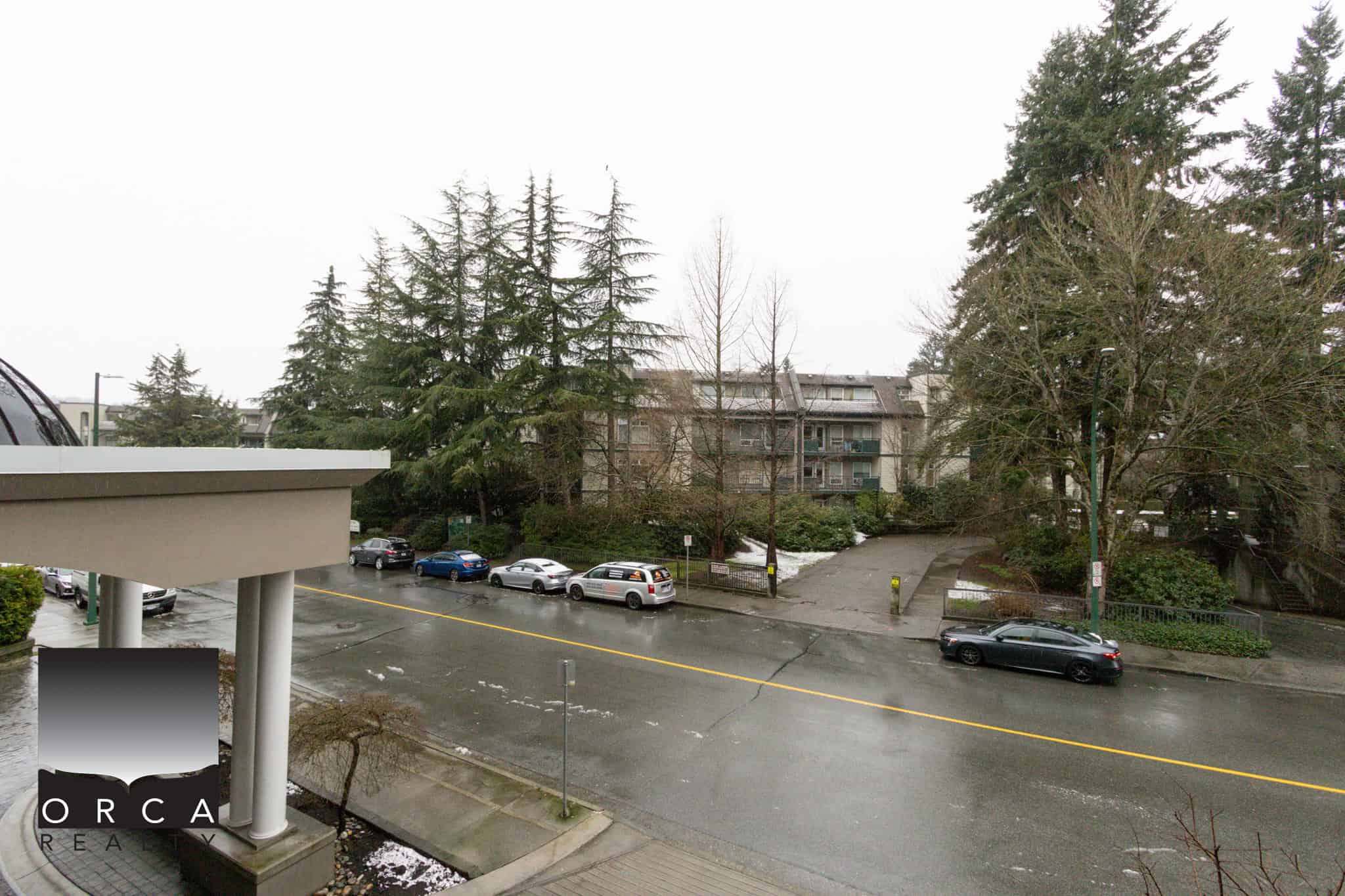 View of Pacific Street in Coquitlam with residential buildings and parked cars on a rainy day.