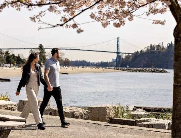 Beautiful couple walking along the waterfront at Uplands Way, West Vancouver, with scenic views of the water and bridge in the background.