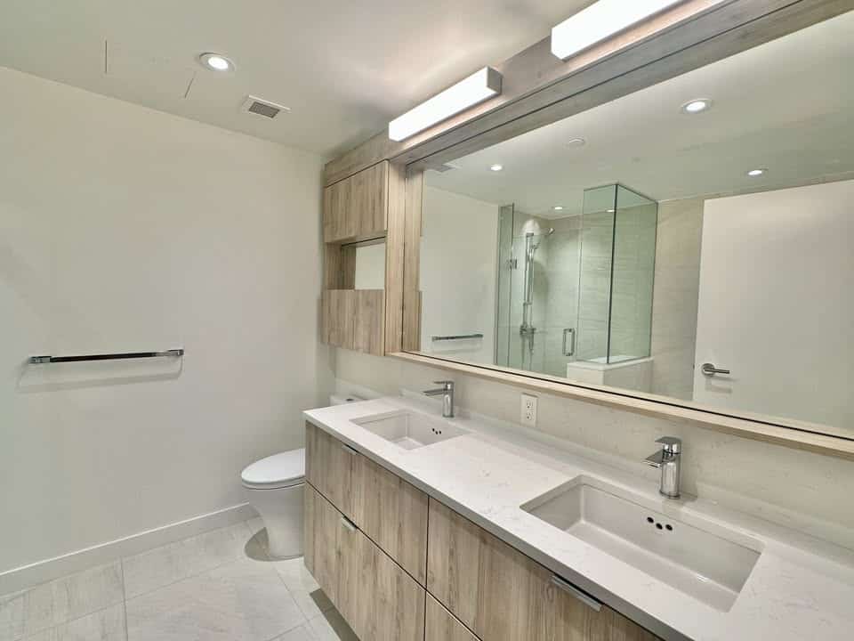 Bright, contemporary bathroom featuring a double vanity with sleek white countertops, stylish wooden cabinetry, and a spacious glass-enclosed shower in North Vancouver.