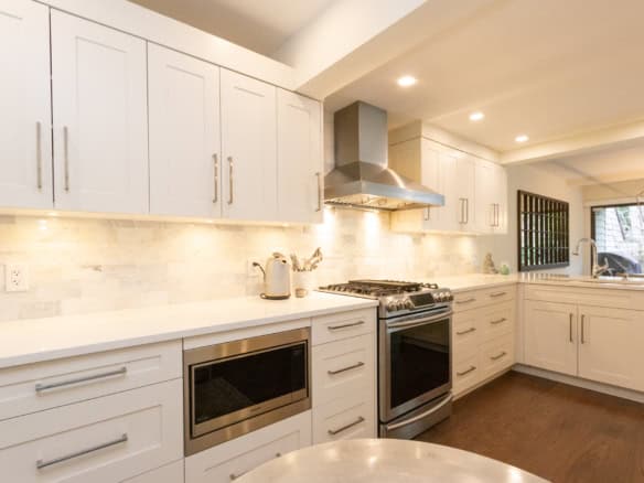 Bright and spacious kitchen in West Vancouver featuring white cabinetry, stainless steel stove and microwave, and elegant backsplash, perfect for luxury home living.
