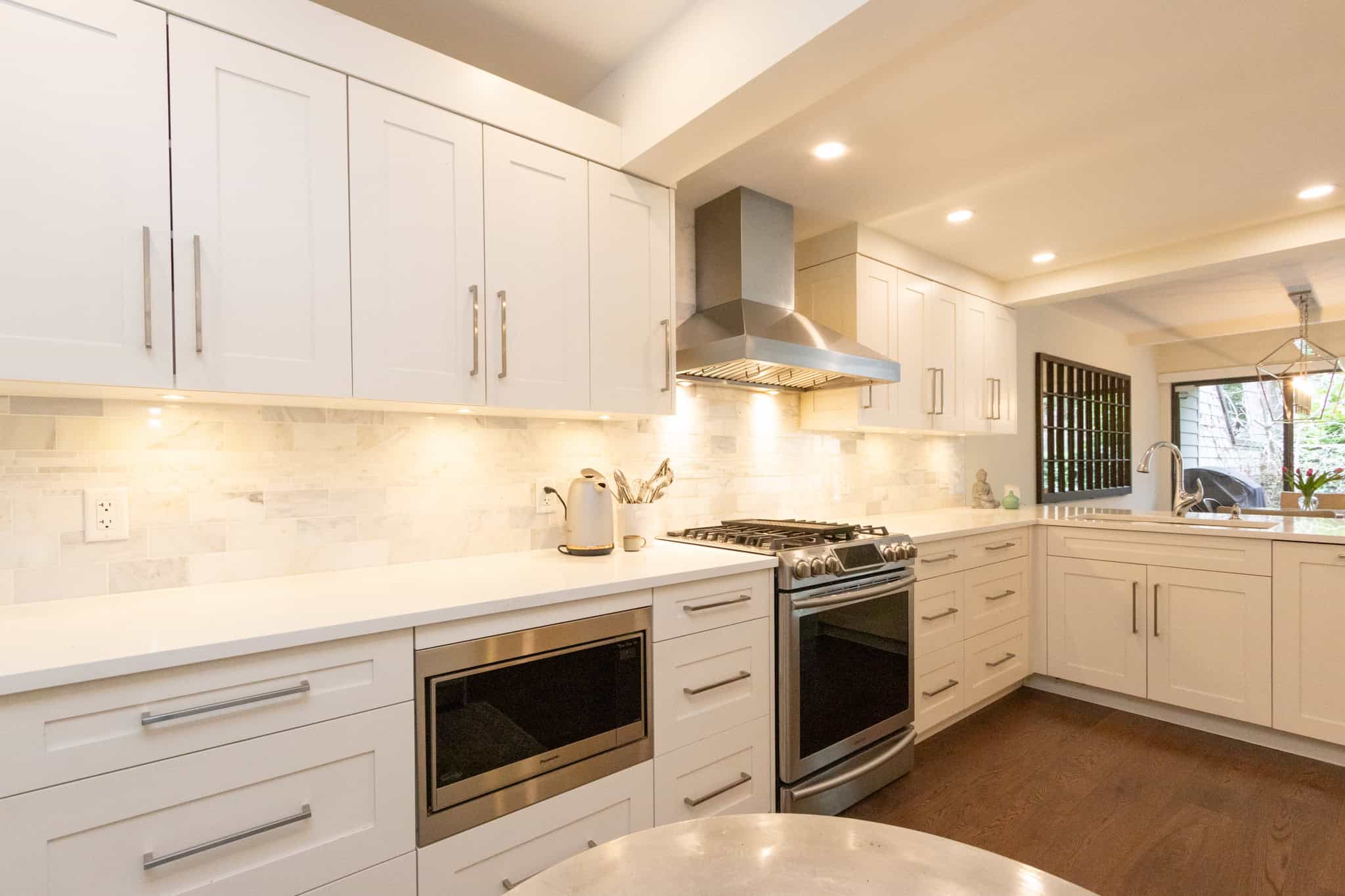Bright and spacious kitchen in West Vancouver featuring white cabinetry, stainless steel stove and microwave, and elegant backsplash, perfect for luxury home living.