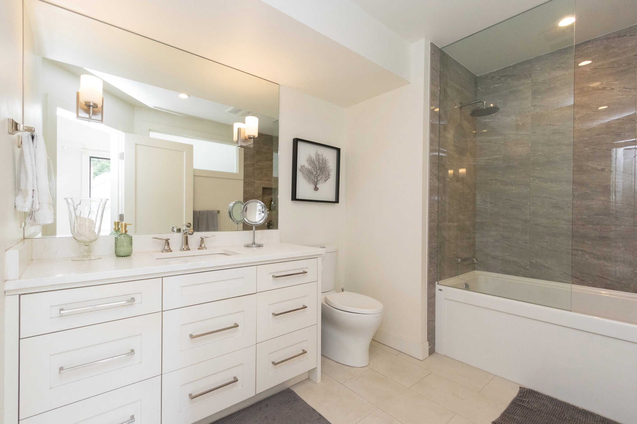 Modern West Vancouver Bathroom with Bathtub and Vanity Bright West Vancouver bathroom featuring a sleek white vanity, large mirror, and a spacious bathtub with glass shower enclosure. Perfect for luxury home living in Marine Drive area.