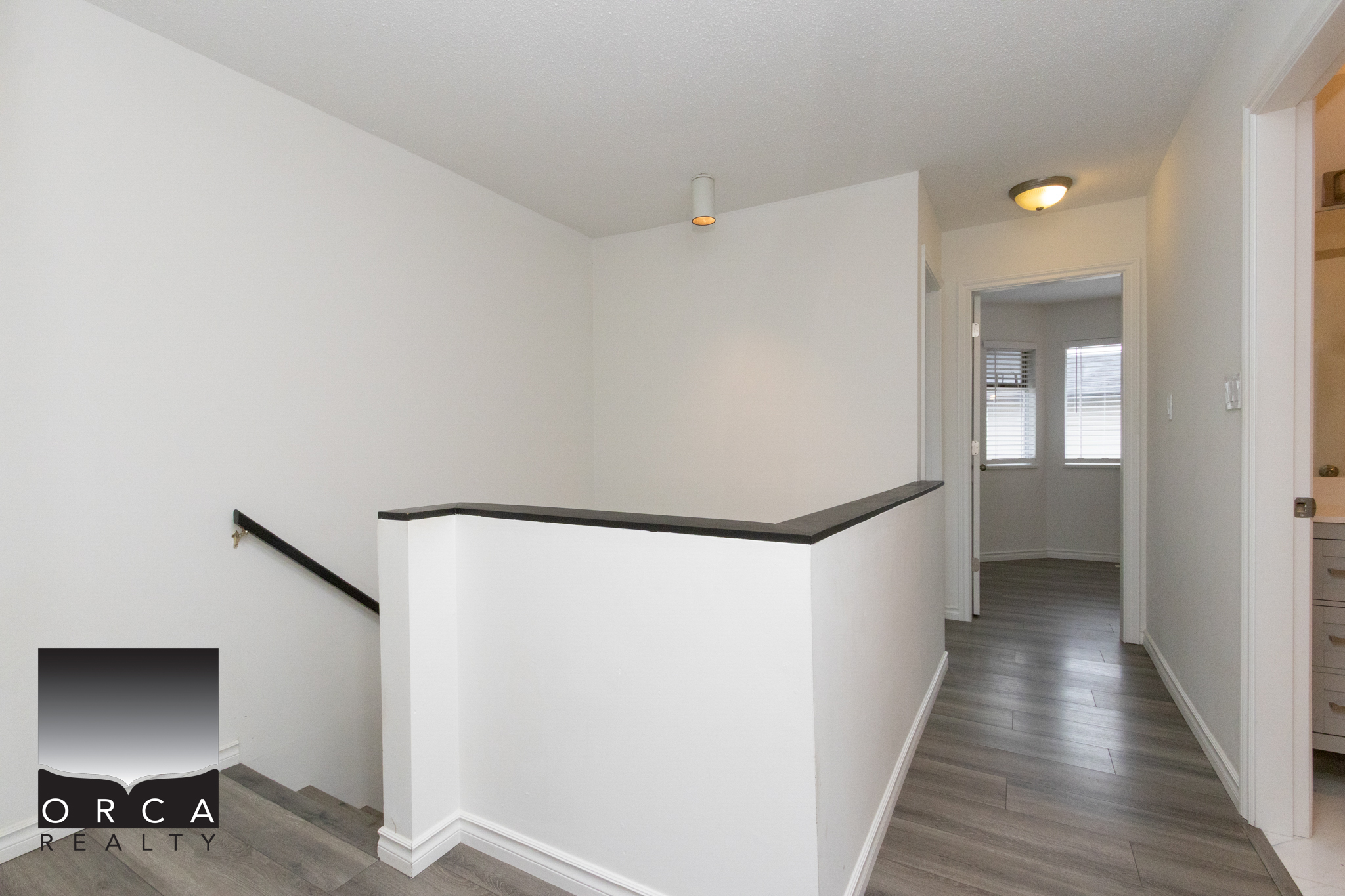 Bright and airy hallway with white walls, hardwood flooring, and natural light from windows.