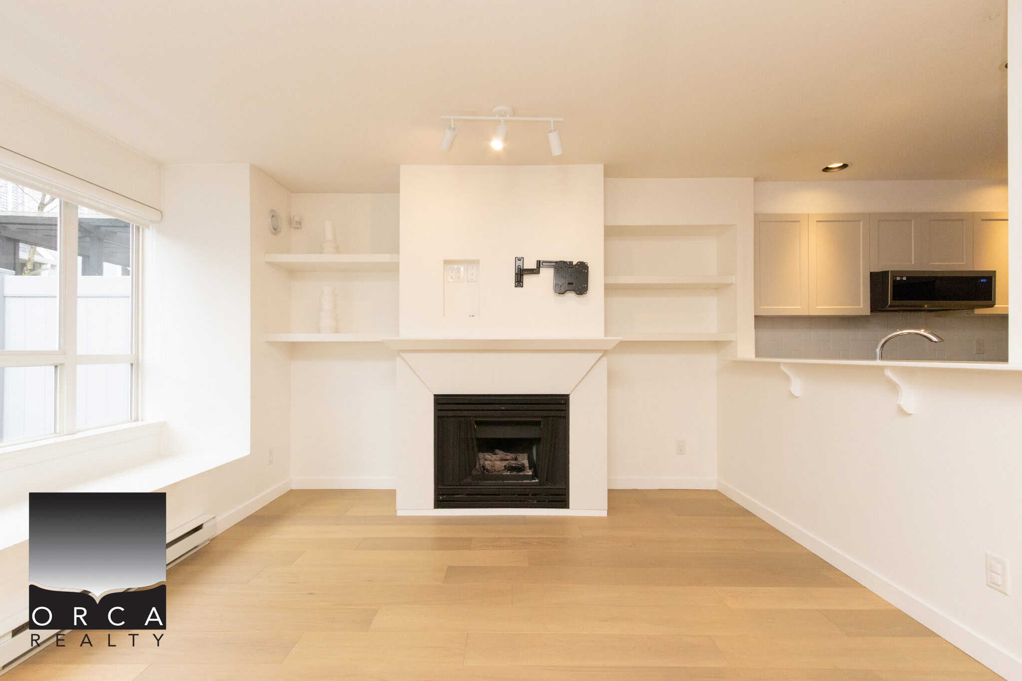 Spacious living room featuring a cozy fireplace, large windows allowing abundant natural light, and minimalist white walls, perfect for relaxing or entertaining in Burnaby.