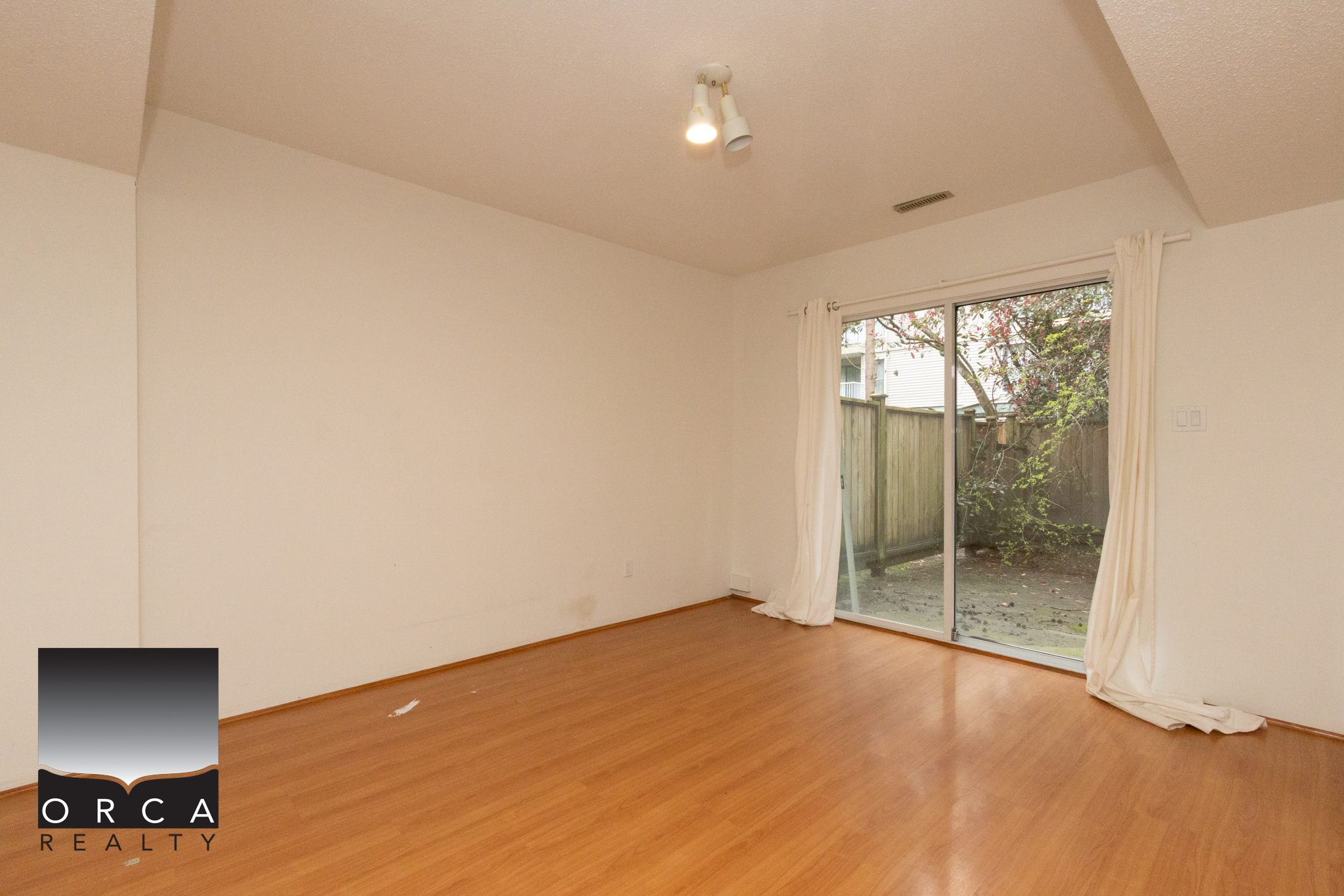 Spacious living room featuring hardwood floors and a large sliding glass door that opens to a private backyard, ideal for family living and entertaining.