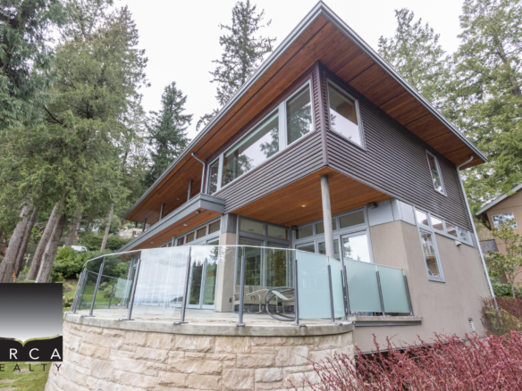 Elegant contemporary house in West Vancouver with large glass windows and a spacious balcony overlooking lush forest surroundings.