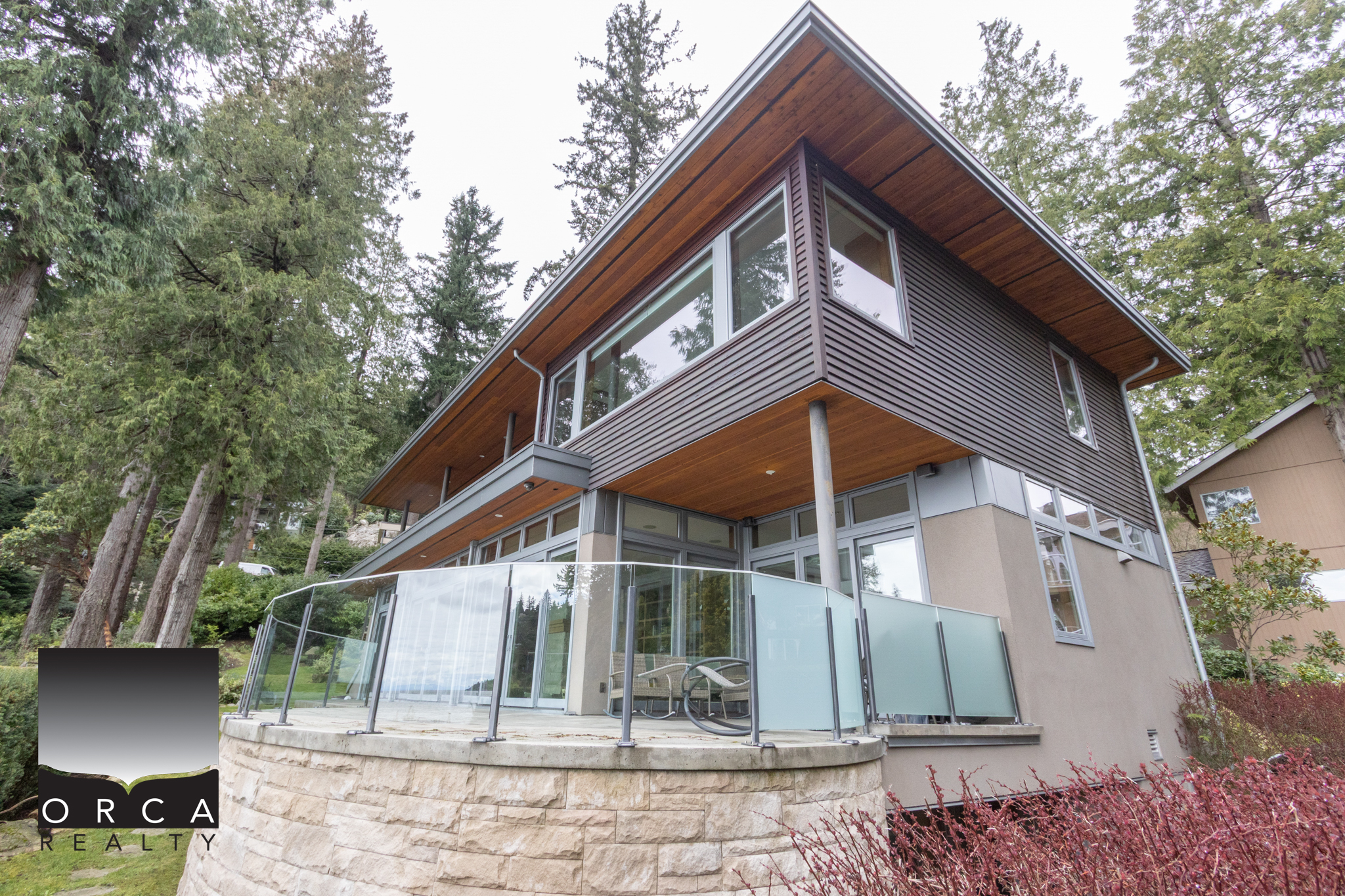 Modern West Vancouver Home with Forest Views Elegant contemporary house in West Vancouver with large glass windows and a spacious balcony overlooking lush forest surroundings.