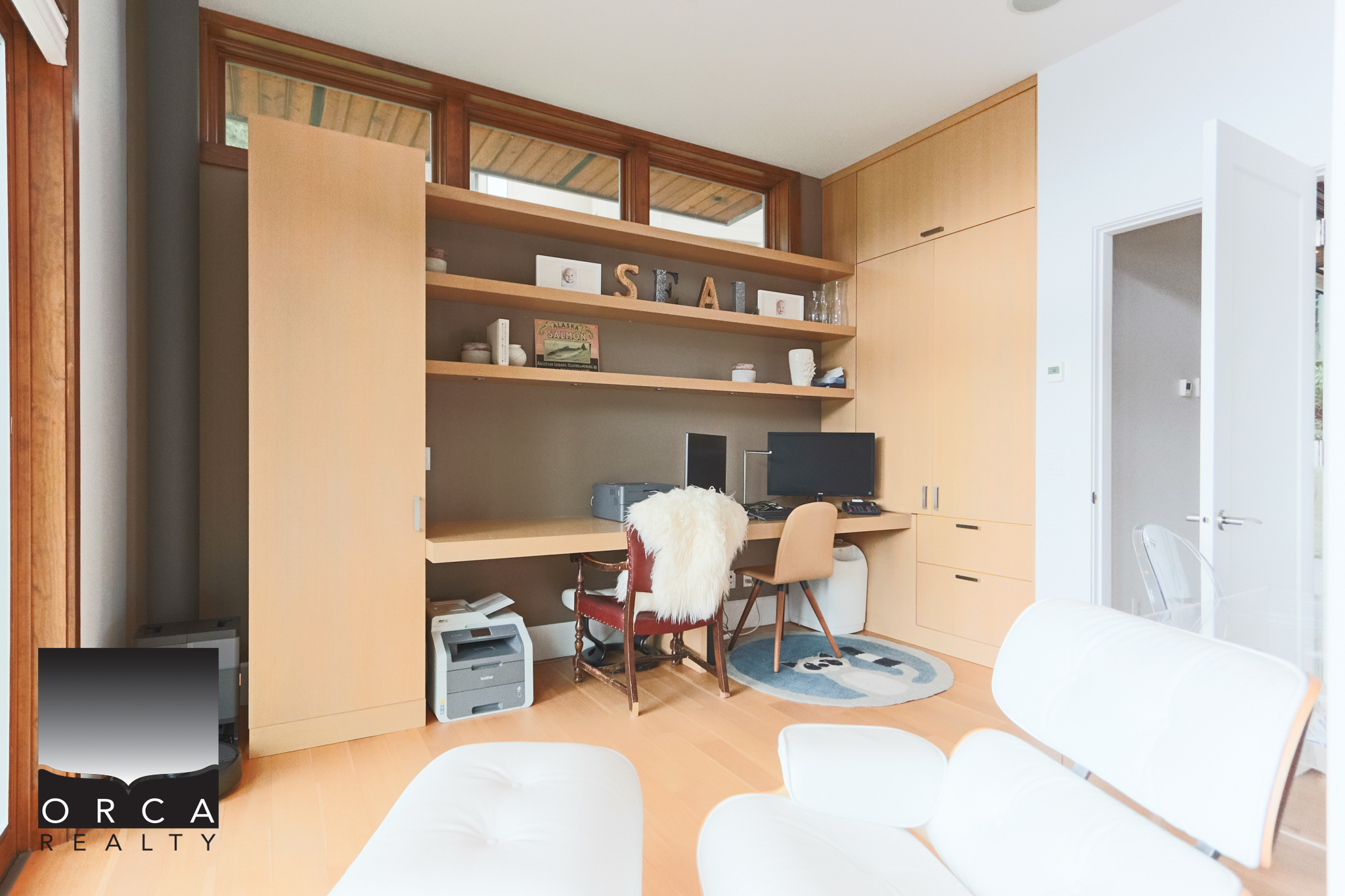 Modern home office with built-in wooden shelves and workspace Spacious home office featuring custom wooden shelving, a desk with dual monitors, and ample storage, perfect for remote work or study in West Vancouver.