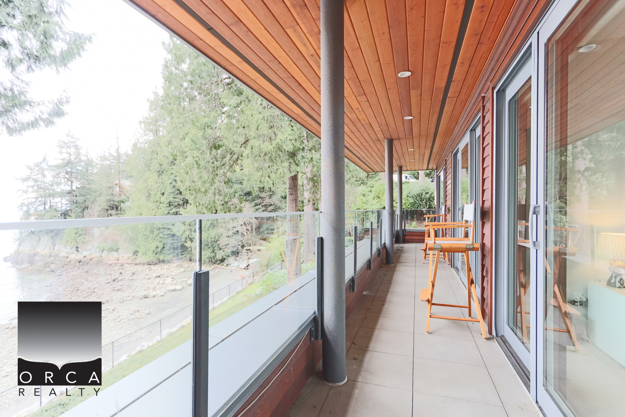 Modern West Vancouver Balcony with Scenic Views Spacious balcony at 6780 Bachelor Bay Place, West Vancouver, showcasing glass railing and natural wood accents, perfect for enjoying outdoor living and stunning waterfront scenery.