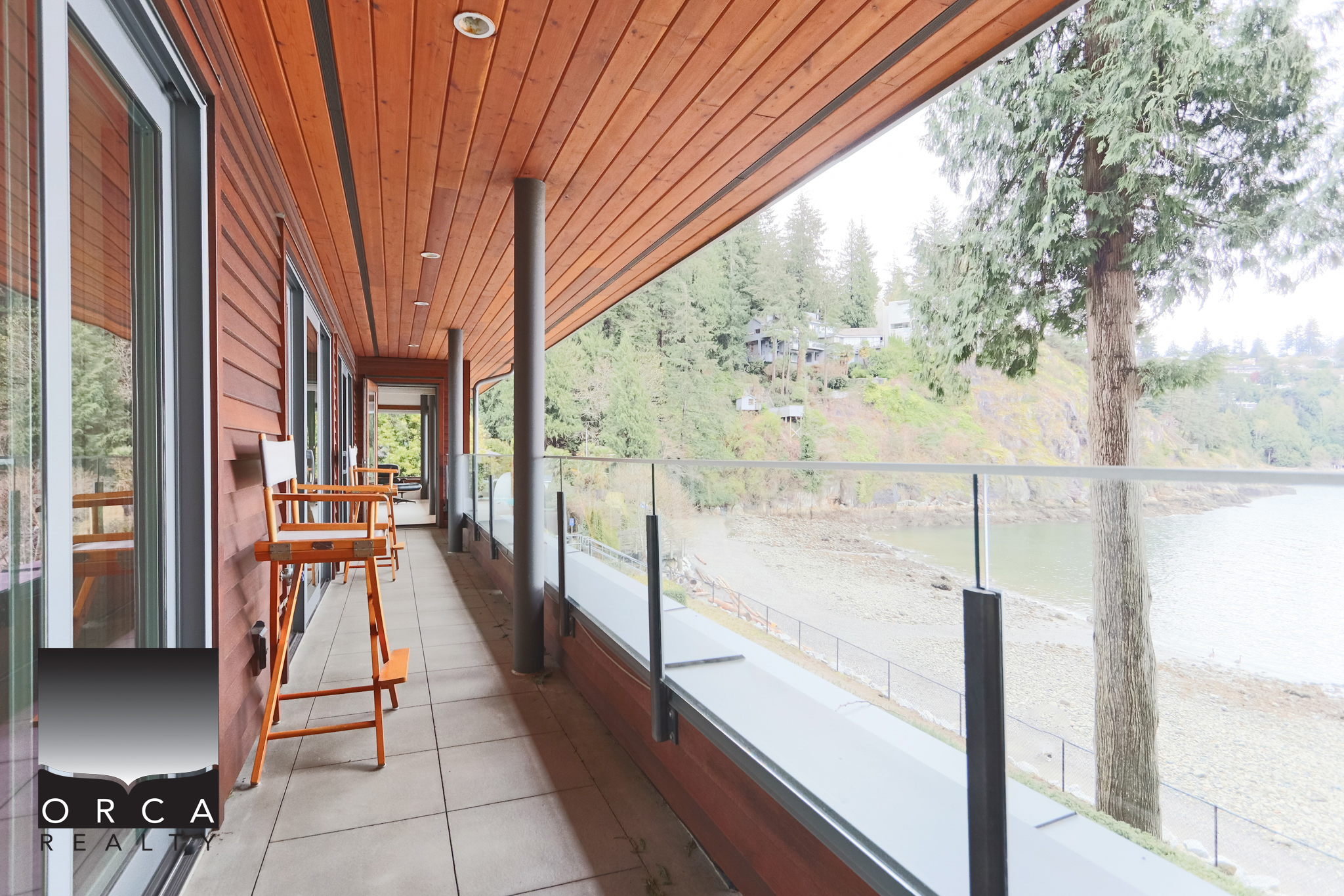 Waterfront Balcony at 6780 Bachelor Bay Place, West Vancouver Waterfront balcony overlooking the ocean at 6780 Bachelor Bay Place, West Vancouver, featuring a cozy outdoor seating area with wooden chairs and a glass railing, perfect for enjoying scenic views.