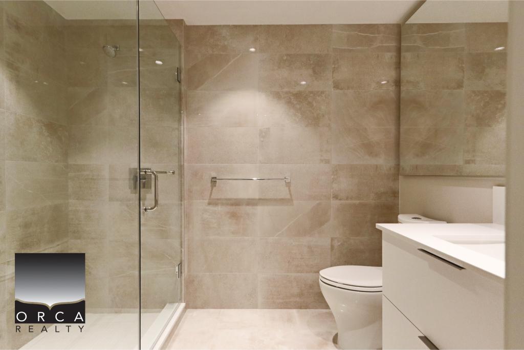 Modern bathroom featuring a glass-enclosed shower, beige tiled walls, and a sleek white vanity with a sink. Perfect for contemporary home interiors and real estate listings.
