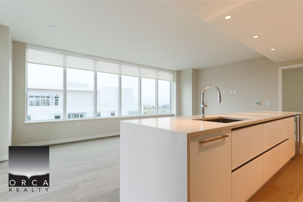Spacious modern kitchen featuring a sleek white island, contemporary fixtures, and expansive windows offering natural light and cityscape views, ideal for urban living.