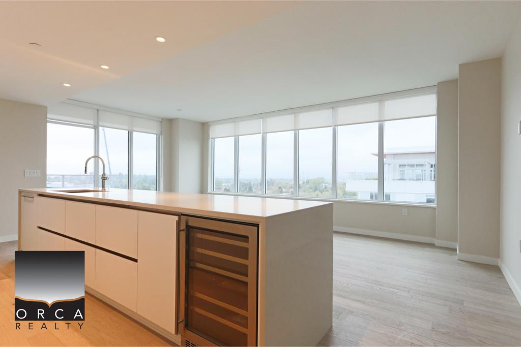 Spacious open-concept kitchen featuring large windows with panoramic city views, sleek white cabinetry, and a built-in wine cooler, ideal for contemporary Vancouver living.