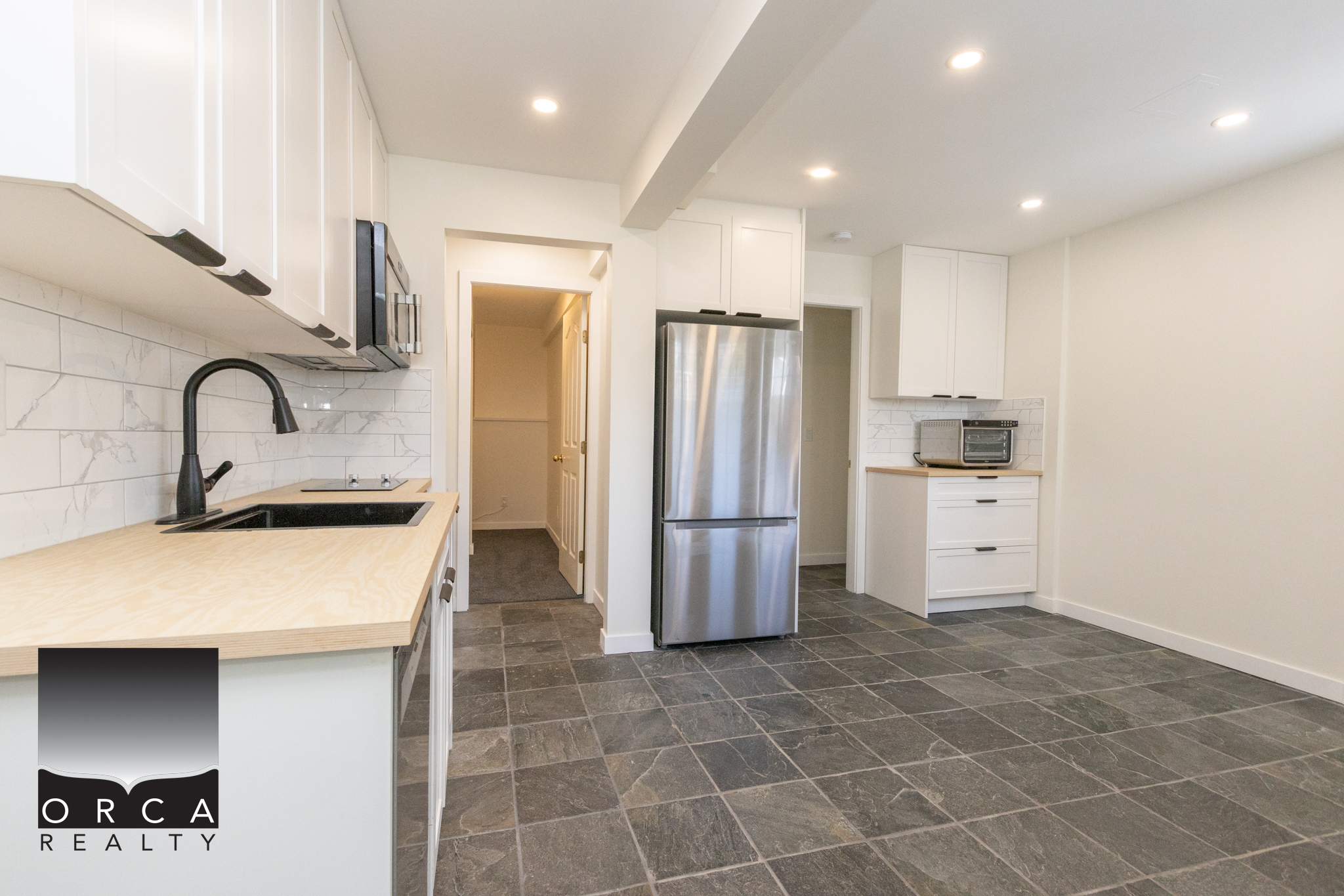 Modern kitchen with white cabinets, stainless steel refrigerator, microwave, and black faucet, featuring a spacious open layout with tiled flooring and bright lighting, ideal for contemporary living.