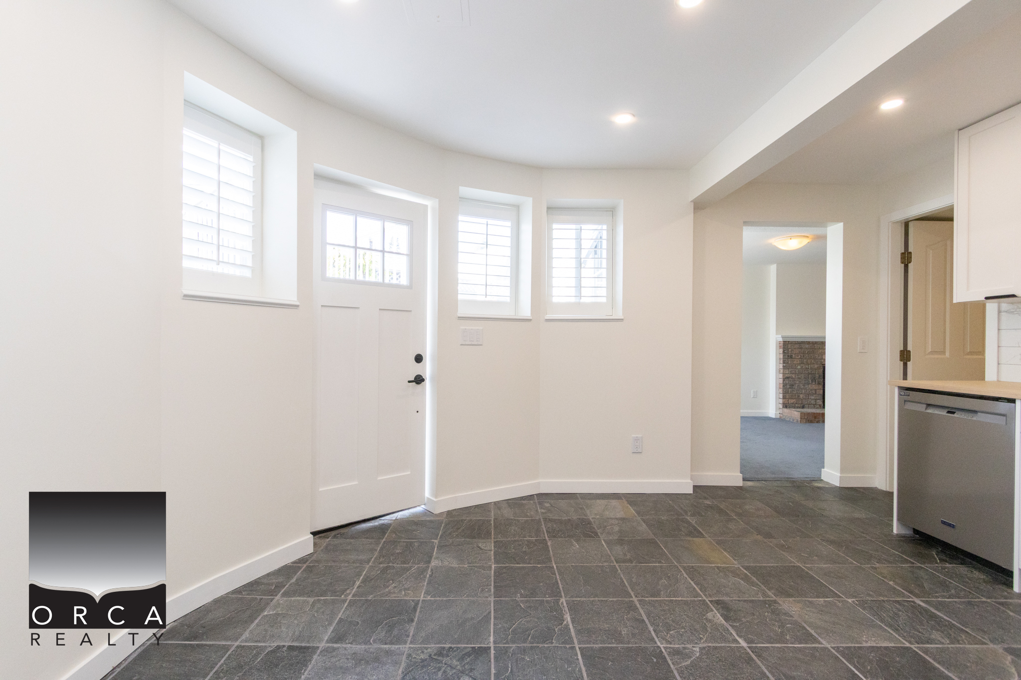 A spacious, bright kitchen area with white walls, multiple windows with shutters, and modern flooring, showcasing a clean and inviting interior design.