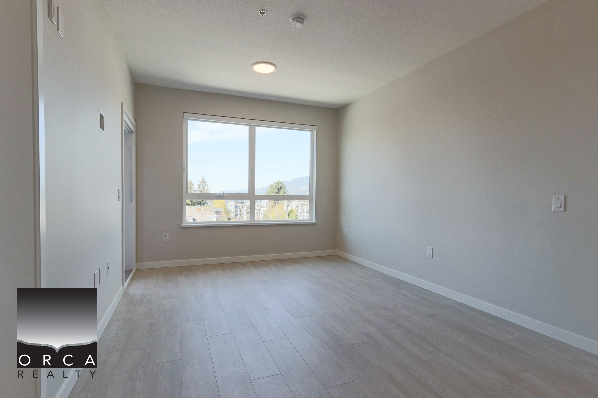 Modern Empty Room with Large Window Bright, spacious empty room with large window and light wood flooring, ideal for residential living or real estate listings in Victoria, BC.