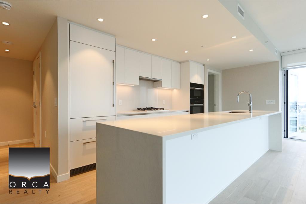 Modern minimalist kitchen with white cabinets and large island, featuring sleek design and ample natural light, ideal for contemporary home living.