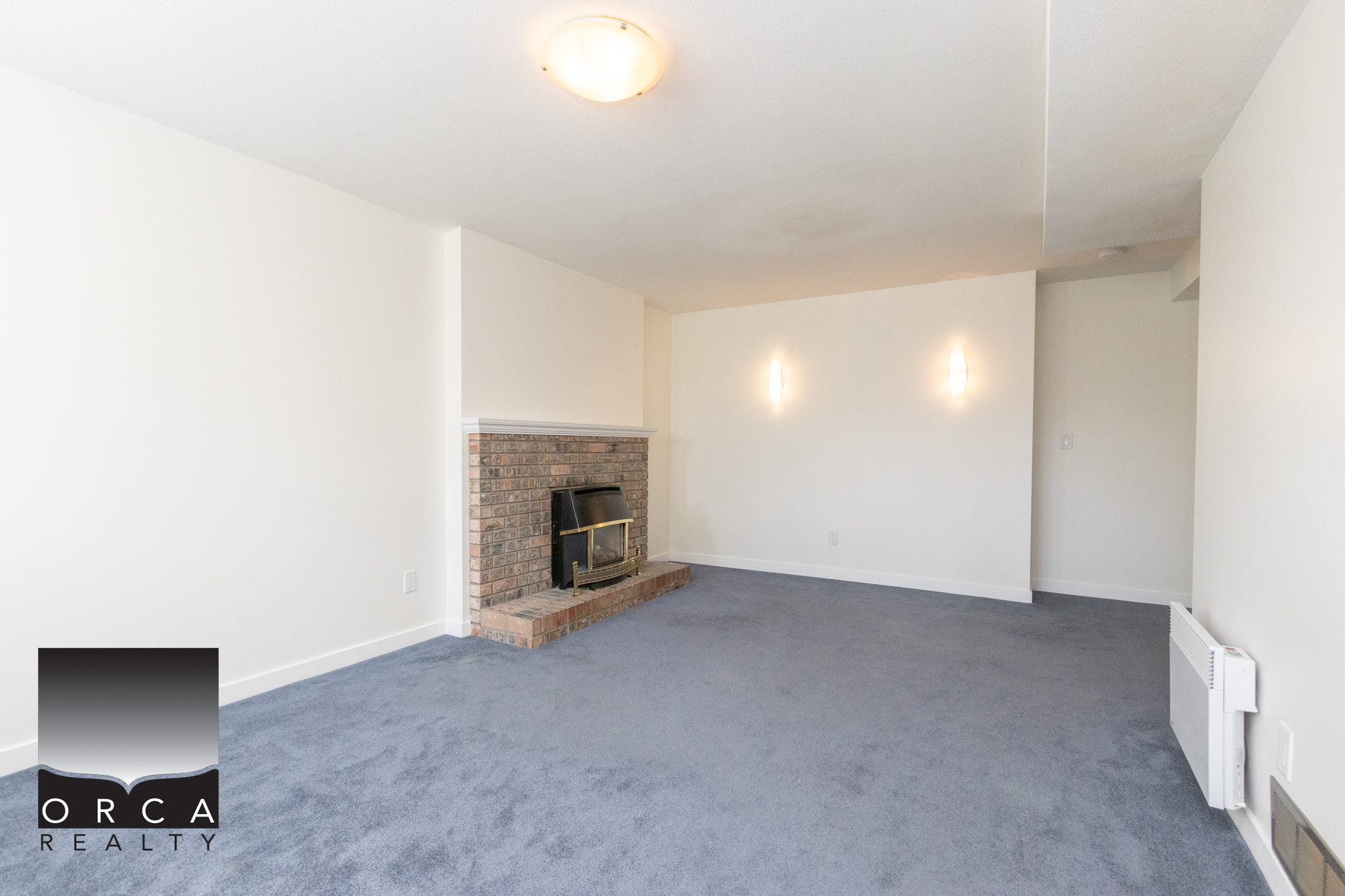 A detailed living room interior with a brick fireplace, white walls, and blue carpet flooring, showcasing a clean and modern residential space for potential homebuyers or renters.