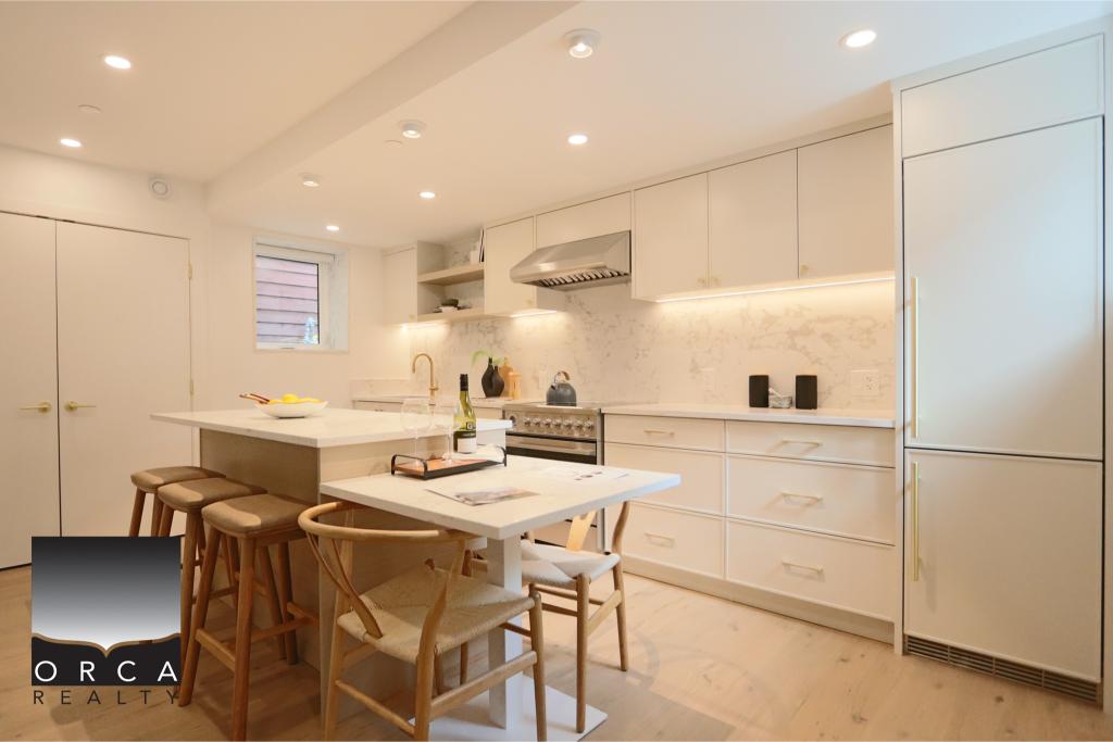 Bright, modern kitchen featuring white cabinetry, a central island with seating, and stainless steel appliances, ideal for contemporary home living.