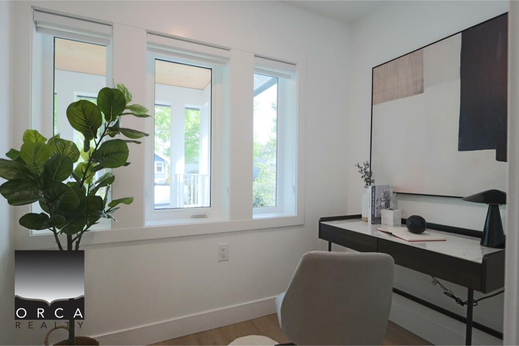 Bright home office featuring large windows, a sleek black desk, and a comfortable chair, ideal for remote work or study. The space is decorated with contemporary art and a lush potted plant, creating.