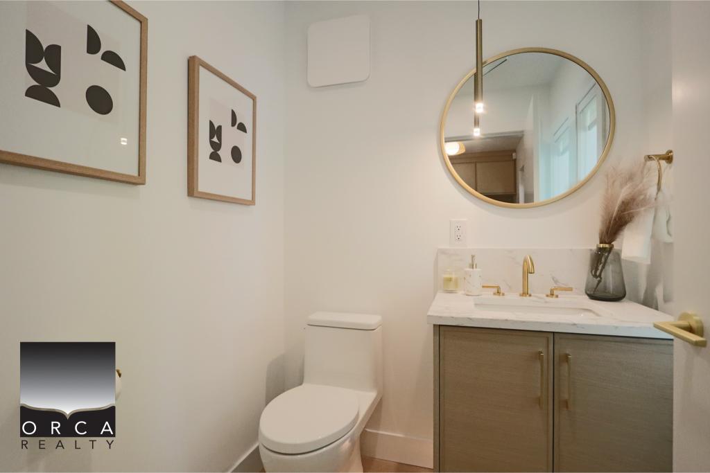 Bright and clean bathroom featuring a white toilet, a stylish vanity with gold hardware, and a large round mirror. Minimalist decor with framed abstract art, perfect for contemporary home interiors.