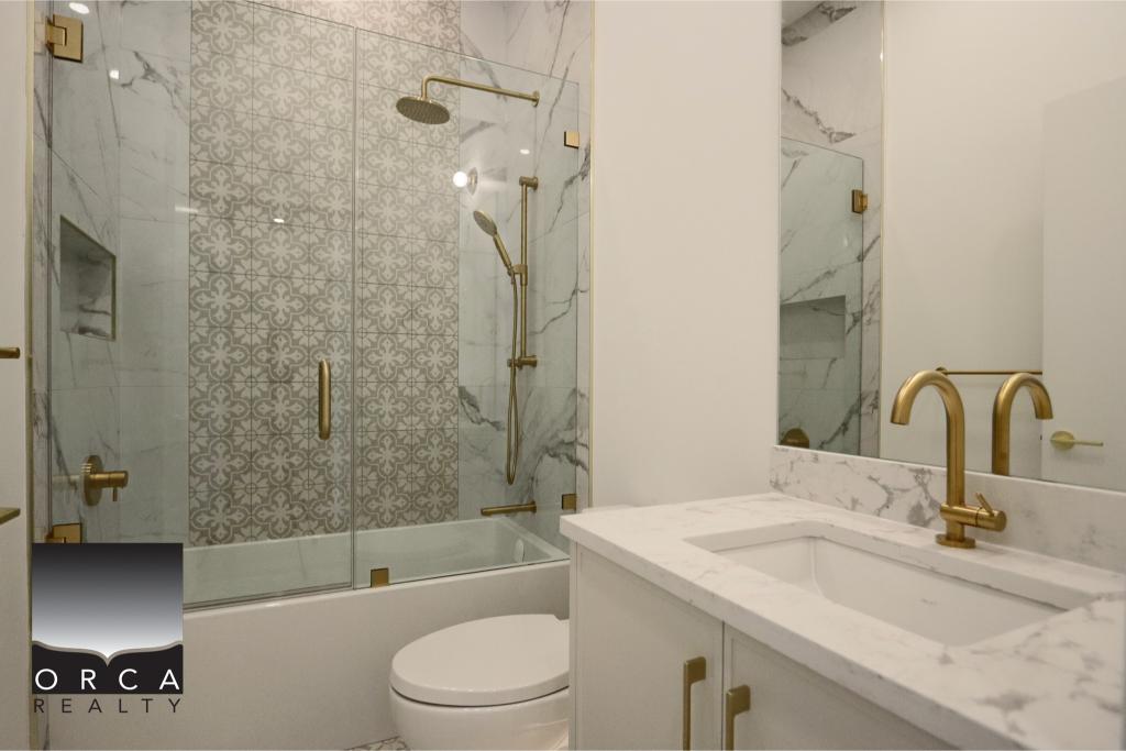 Luxurious bathroom featuring marble countertops, gold fixtures, and a glass-enclosed shower with decorative tile accents.
