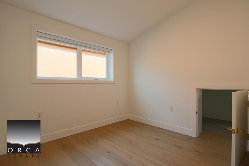 Bright, empty bedroom featuring a large window and light wood flooring, ideal for new homeowners or renters seeking a cozy, well-lit space in a residential property.