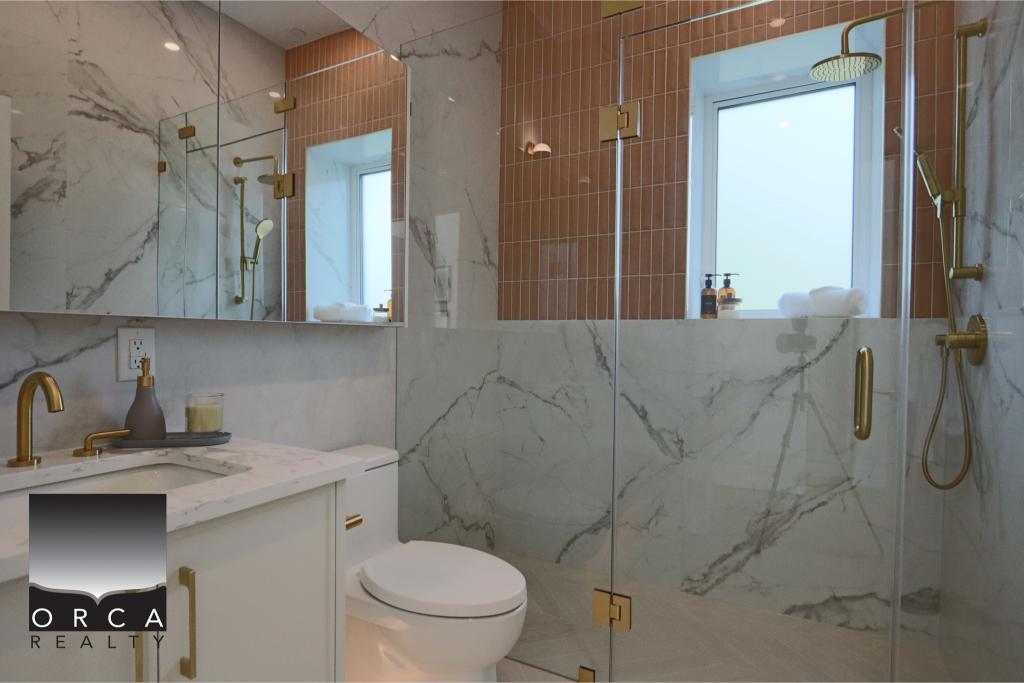 Elegant bathroom featuring marble walls and gold fixtures, including a walk-in shower and vanity, with a frosted window for natural light.