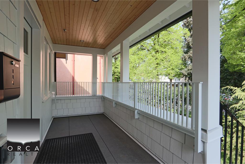Bright balcony with white railing and wooden ceiling, overlooking lush green trees, perfect for relaxing or outdoor dining.