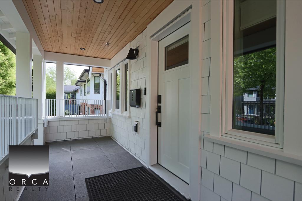 Front porch of a modern home featuring white siding, a white door, black mailbox, and window with greenery outside, showcasing contemporary residential design.