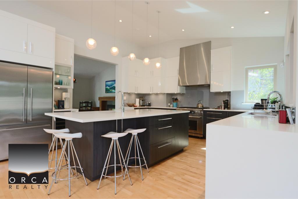 Contemporary kitchen featuring white cabinetry, a black island with seating, stainless steel appliances, and ample natural light, ideal for modern home living.