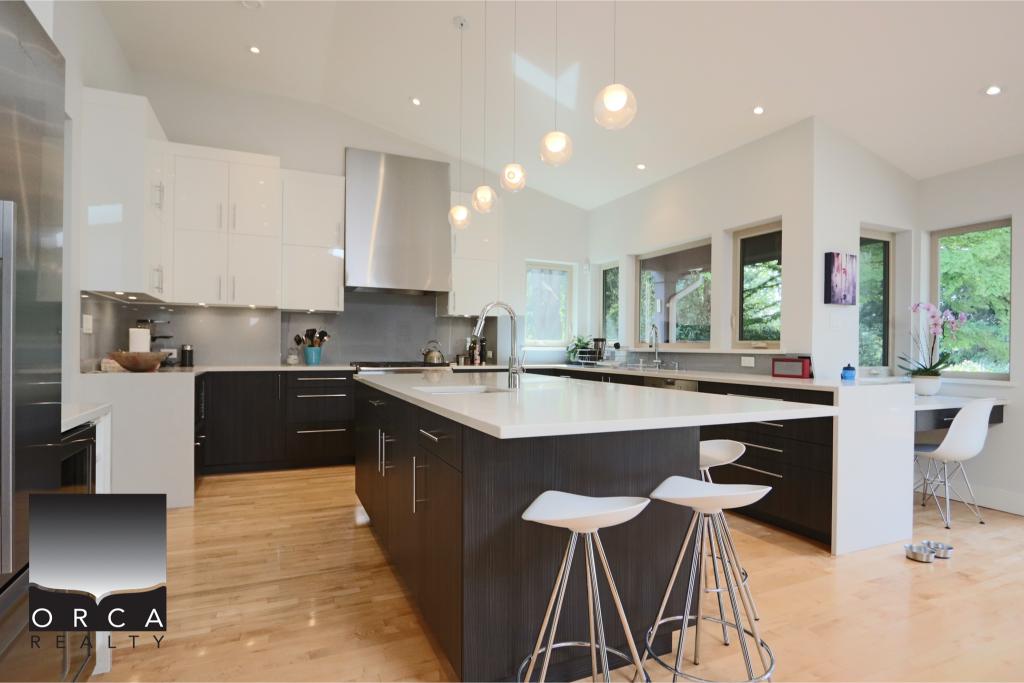 Spacious modern kitchen featuring white and black cabinetry, a central island, and large windows that bring in natural light, perfect for contemporary home living.